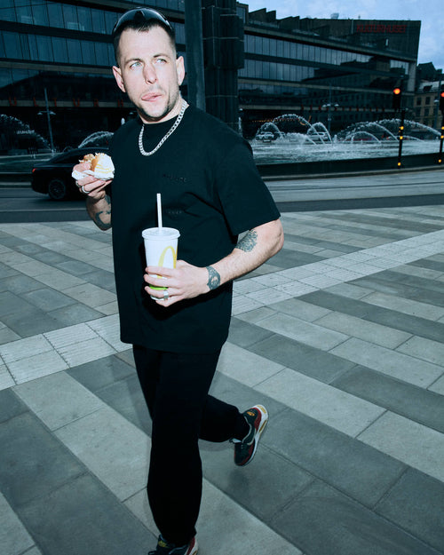 Felix walking on the street eating a hamburger wearing Heavy Jersey T-Shirt in Black