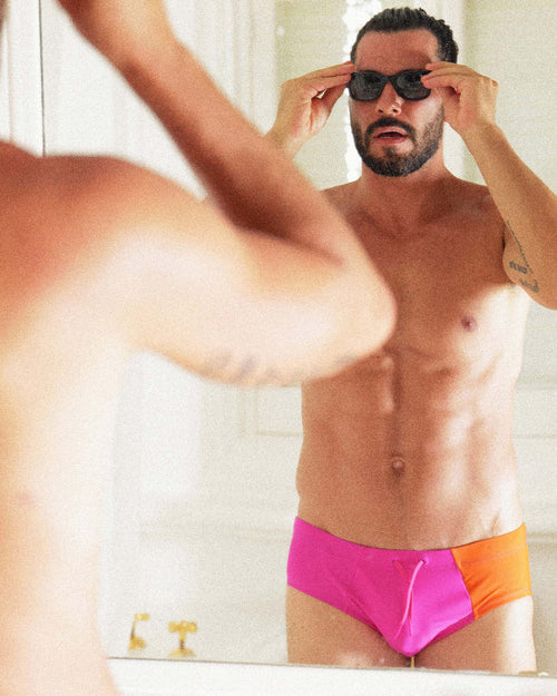 Uriel del Toro looking in the mirror wearing sunglasses and Cuixmala Swim Brief in Fuchsia / Flame